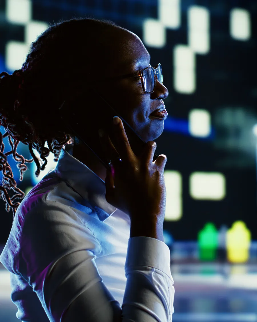 A woman on a call at night, the lights of a city behind her.